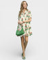 Woman wearing a floral dress holding a green handbag on a white background