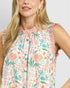 Woman wearing a sleeveless floral top with ruffled edges on a plain background