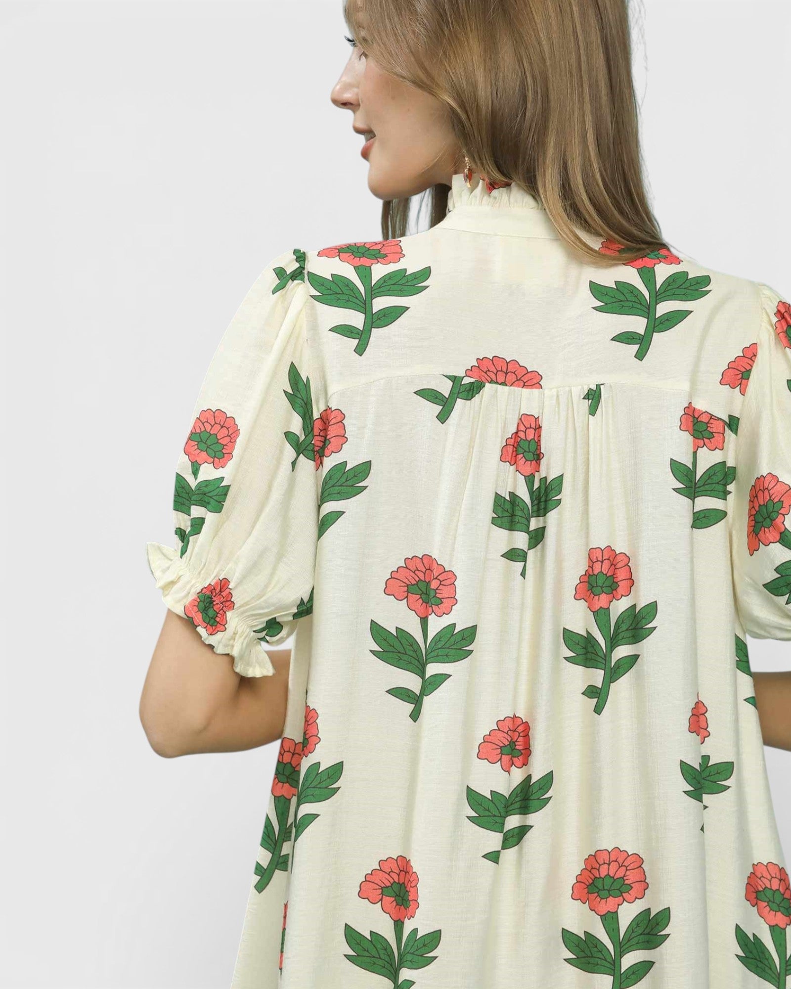 Woman wearing a cream-colored blouse with floral patterns on a plain background
