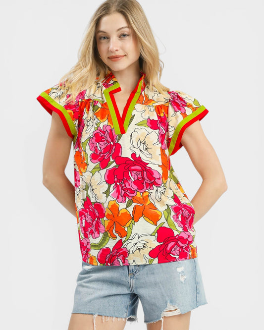 Woman wearing a colorful floral blouse with red and green accents on a white background