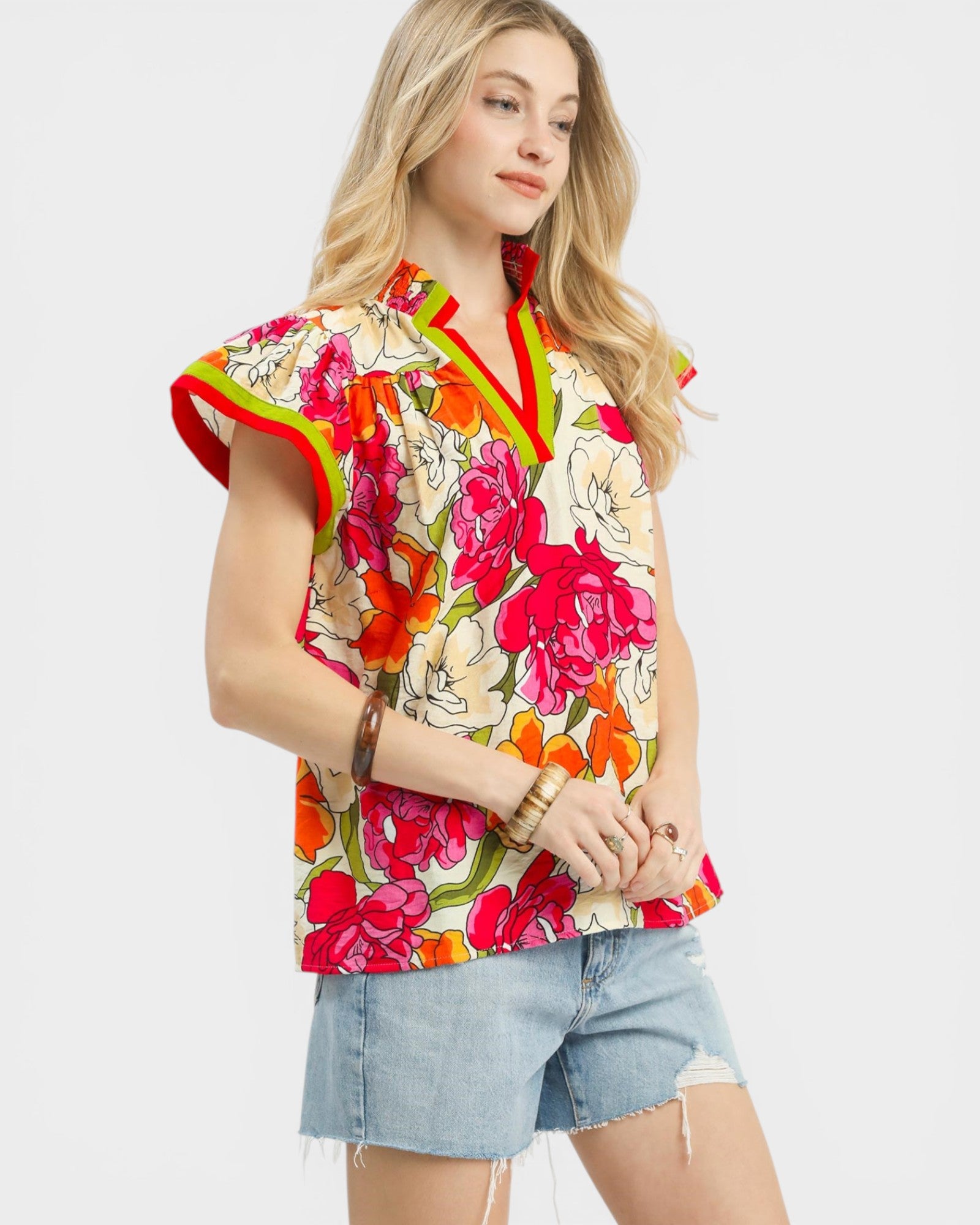 Woman wearing a colorful floral sleeveless top with denim shorts on a white background