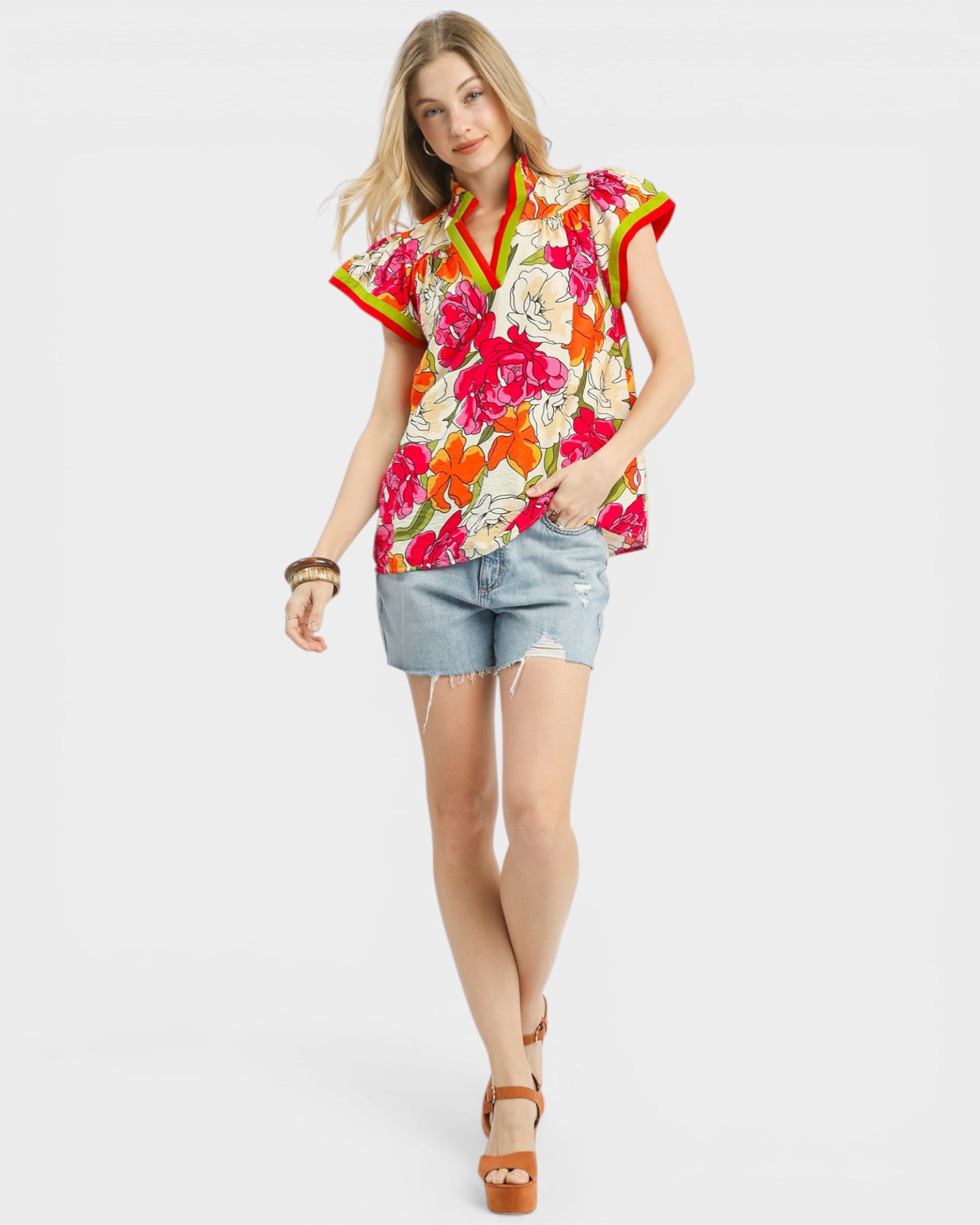Woman wearing a colorful floral blouse and denim shorts on a white background