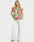 Woman wearing a colorful floral blouse and white pants on a white background