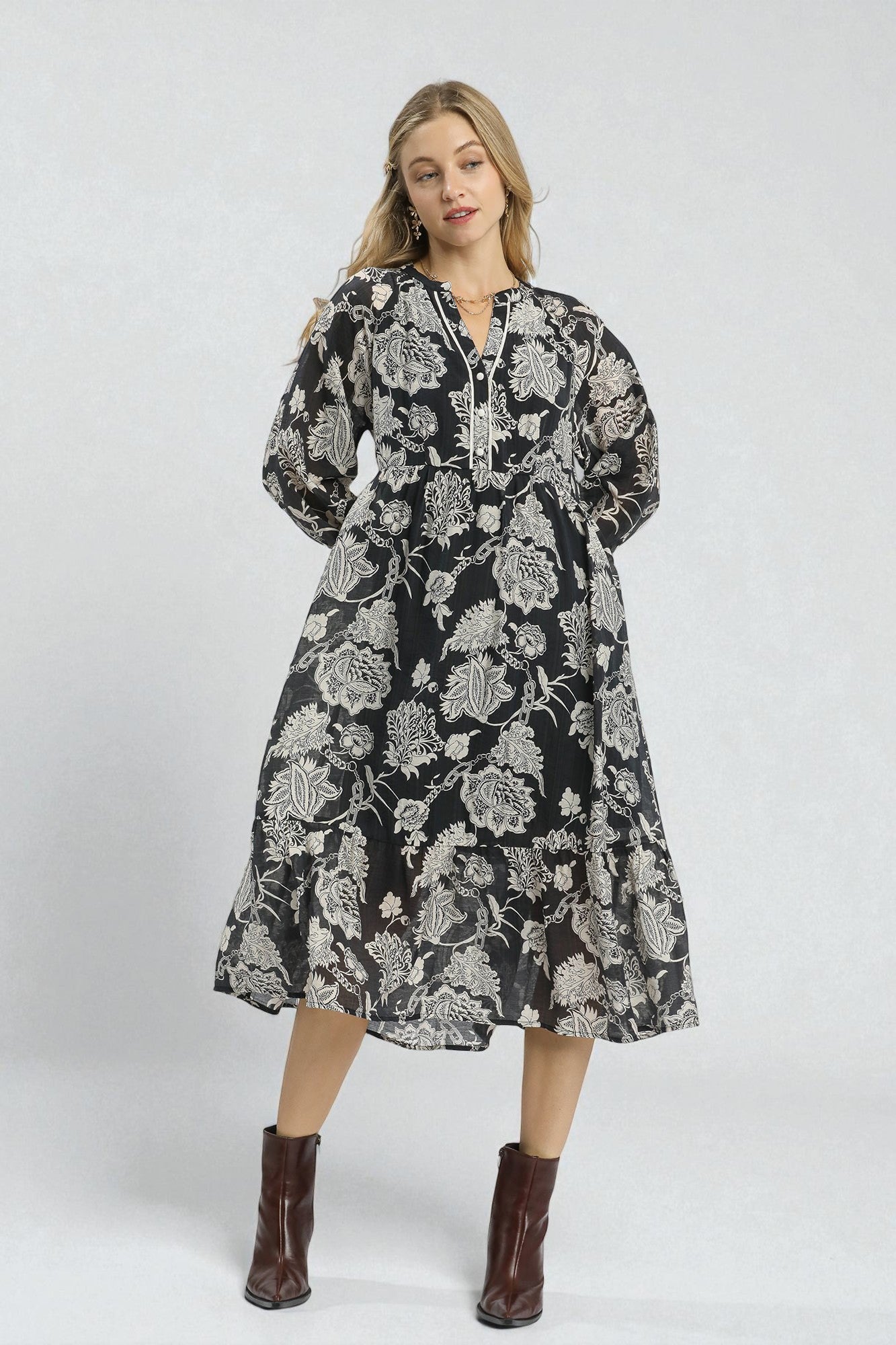 Woman wearing a black floral dress with brown boots on a white background