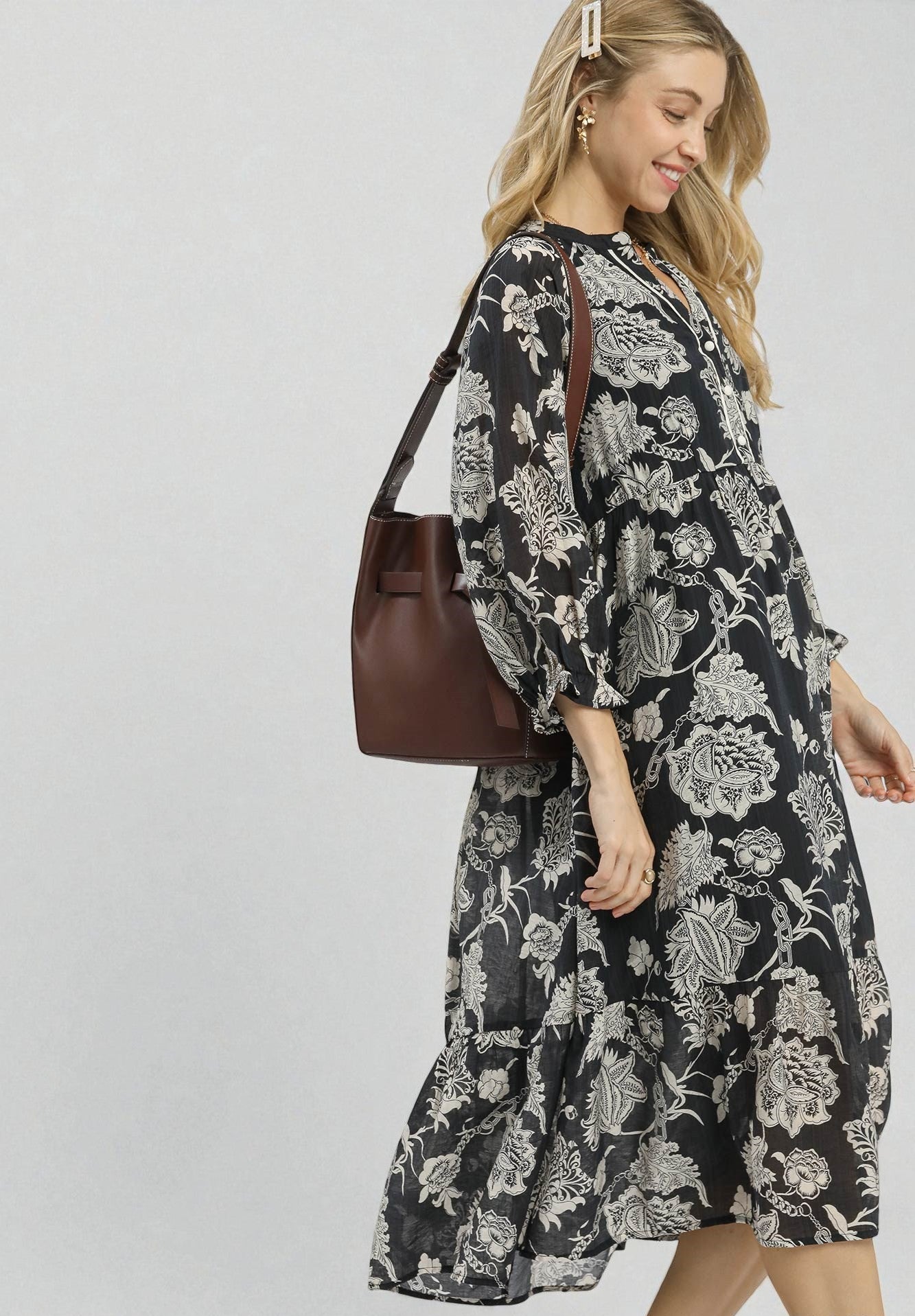 Woman wearing a black floral dress holding a brown handbag on a white background