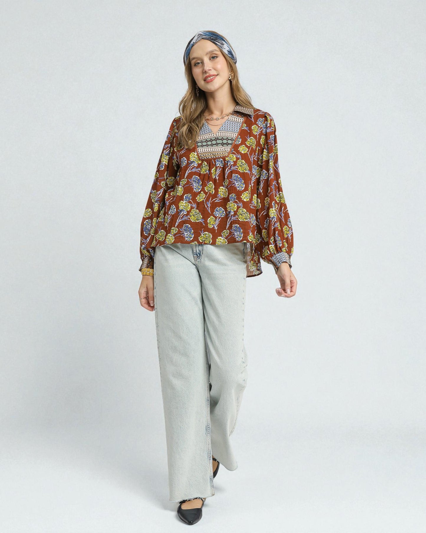 Woman wearing a patterned blouse and light pants on a white background