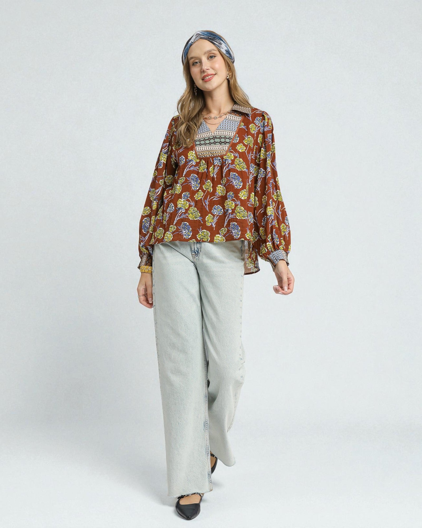 Woman wearing a patterned blouse and light pants on a white background