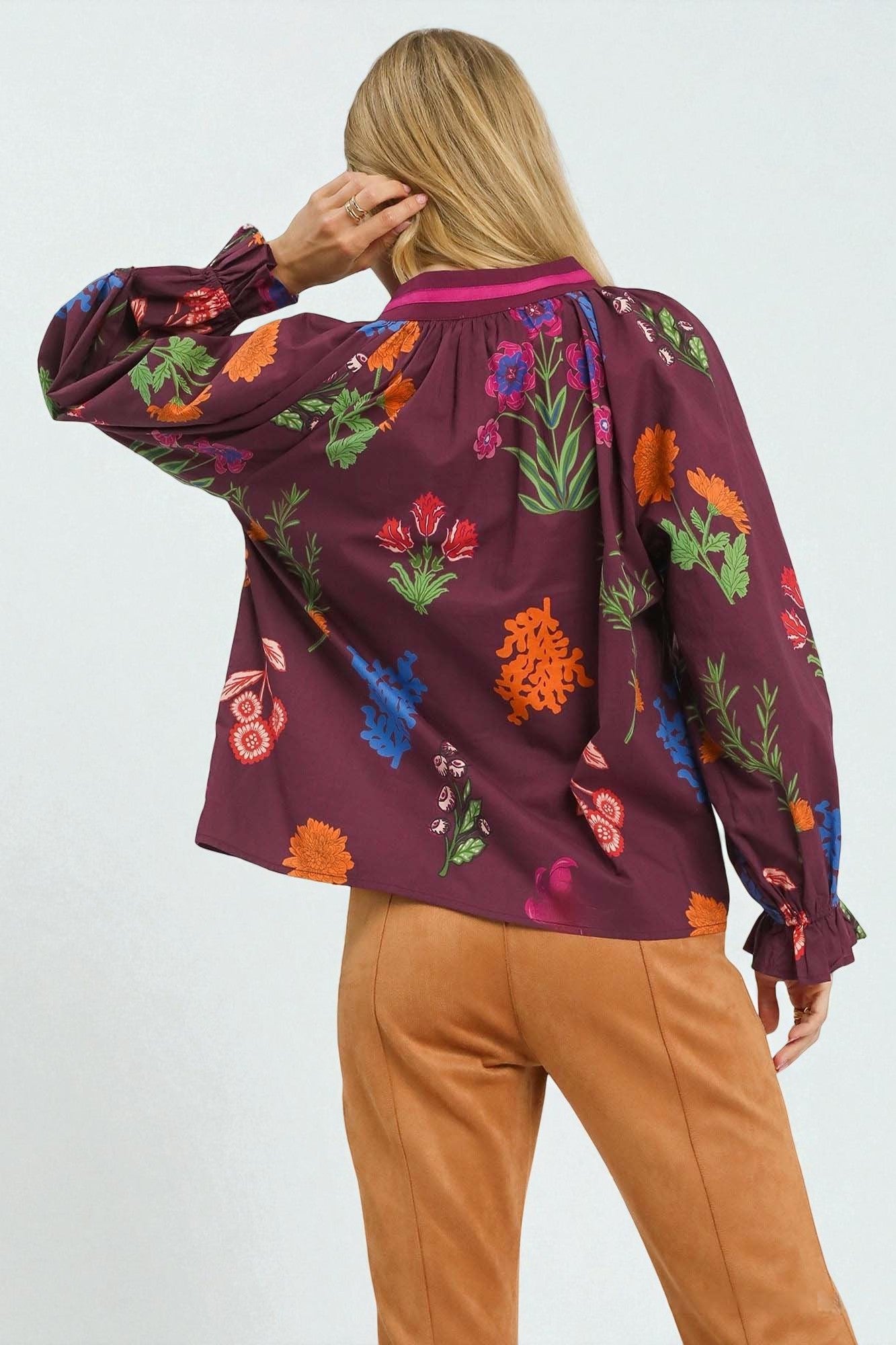 Person wearing a burgundy blouse with colorful floral patterns on a white background