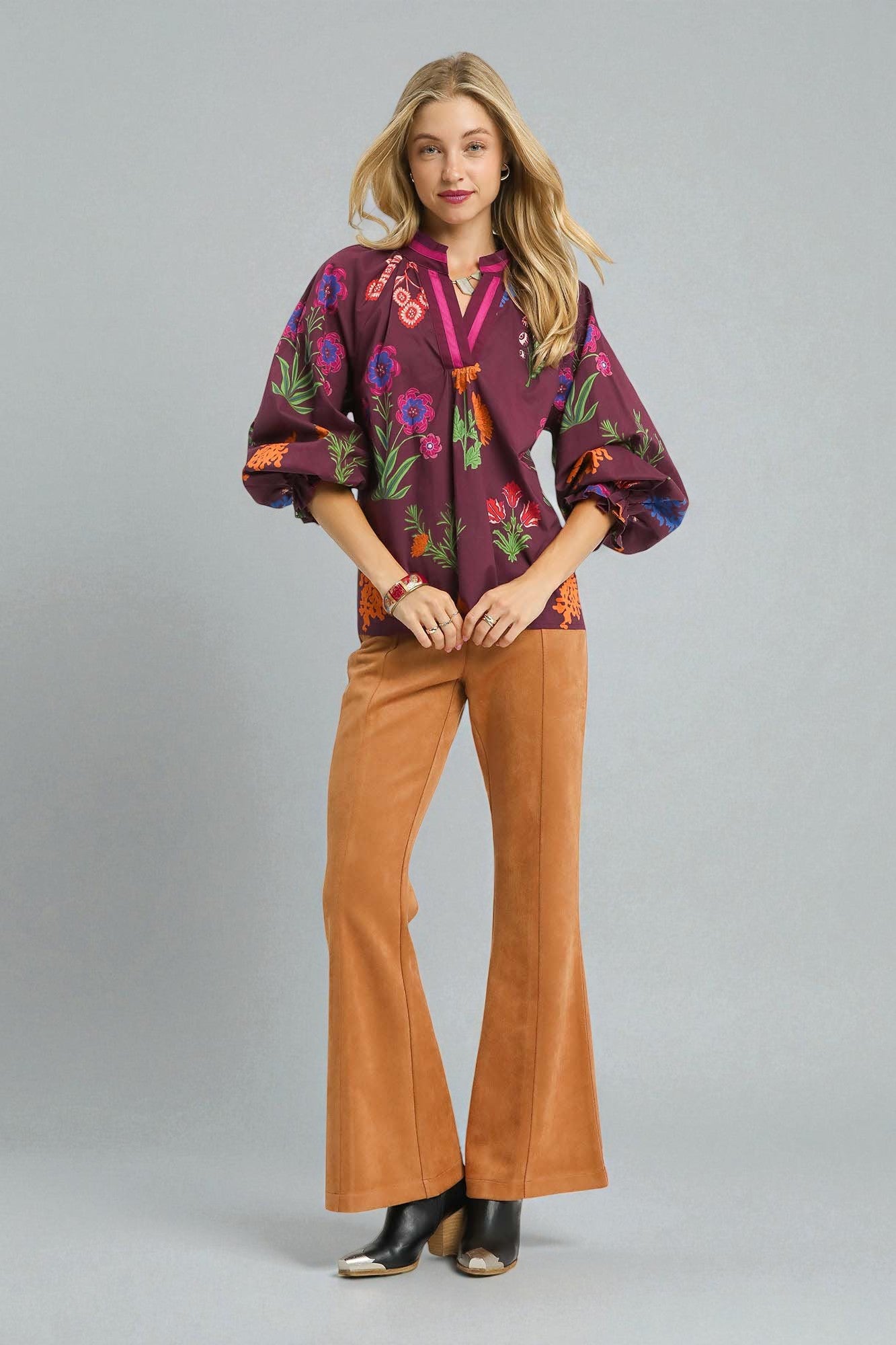 Woman wearing a colorful blouse and brown pants on a gray background