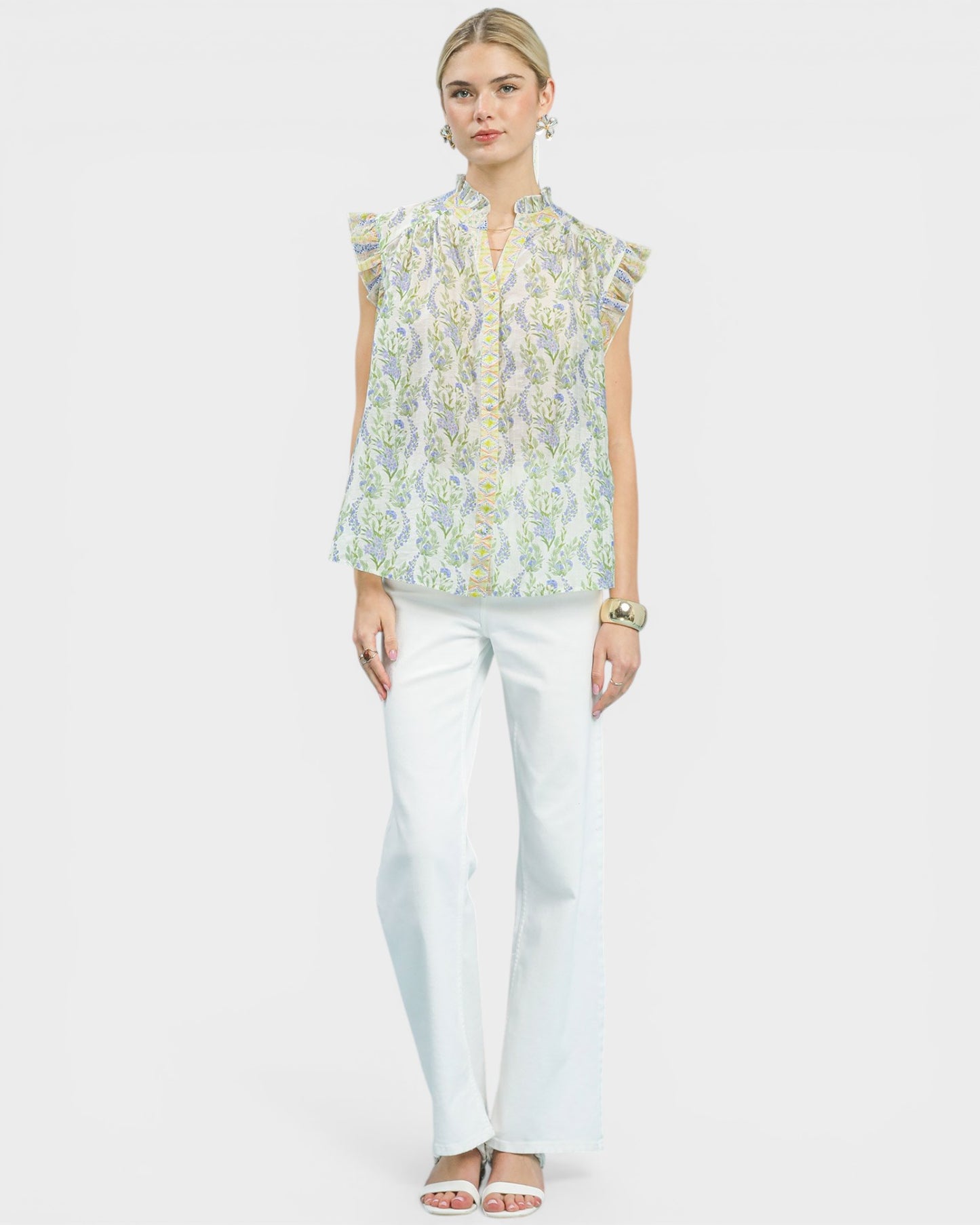 Woman wearing a floral blouse and white pants on a plain background