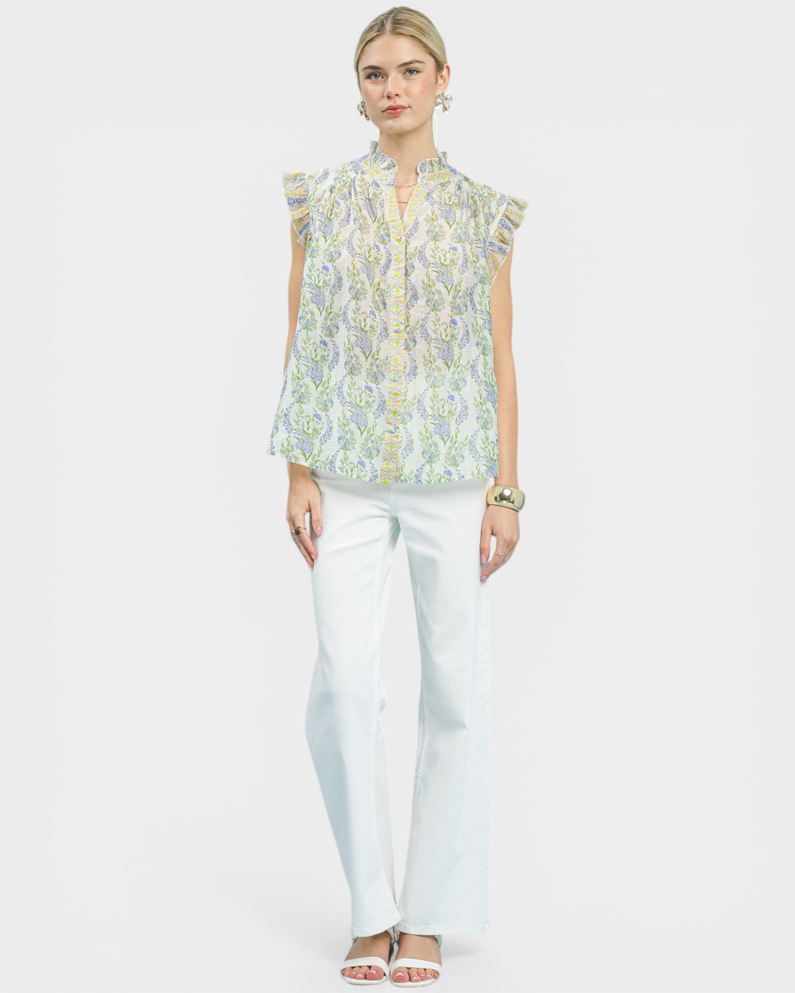 Woman wearing a floral blouse and white pants on a plain background