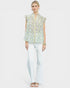 Woman wearing a floral blouse and white pants on a plain background