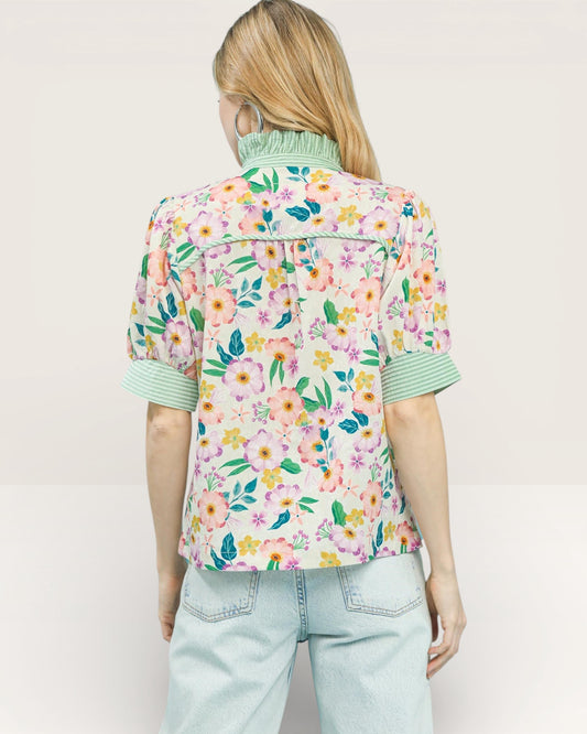 Person wearing a colorful floral shirt with rolled-up sleeves on a plain background