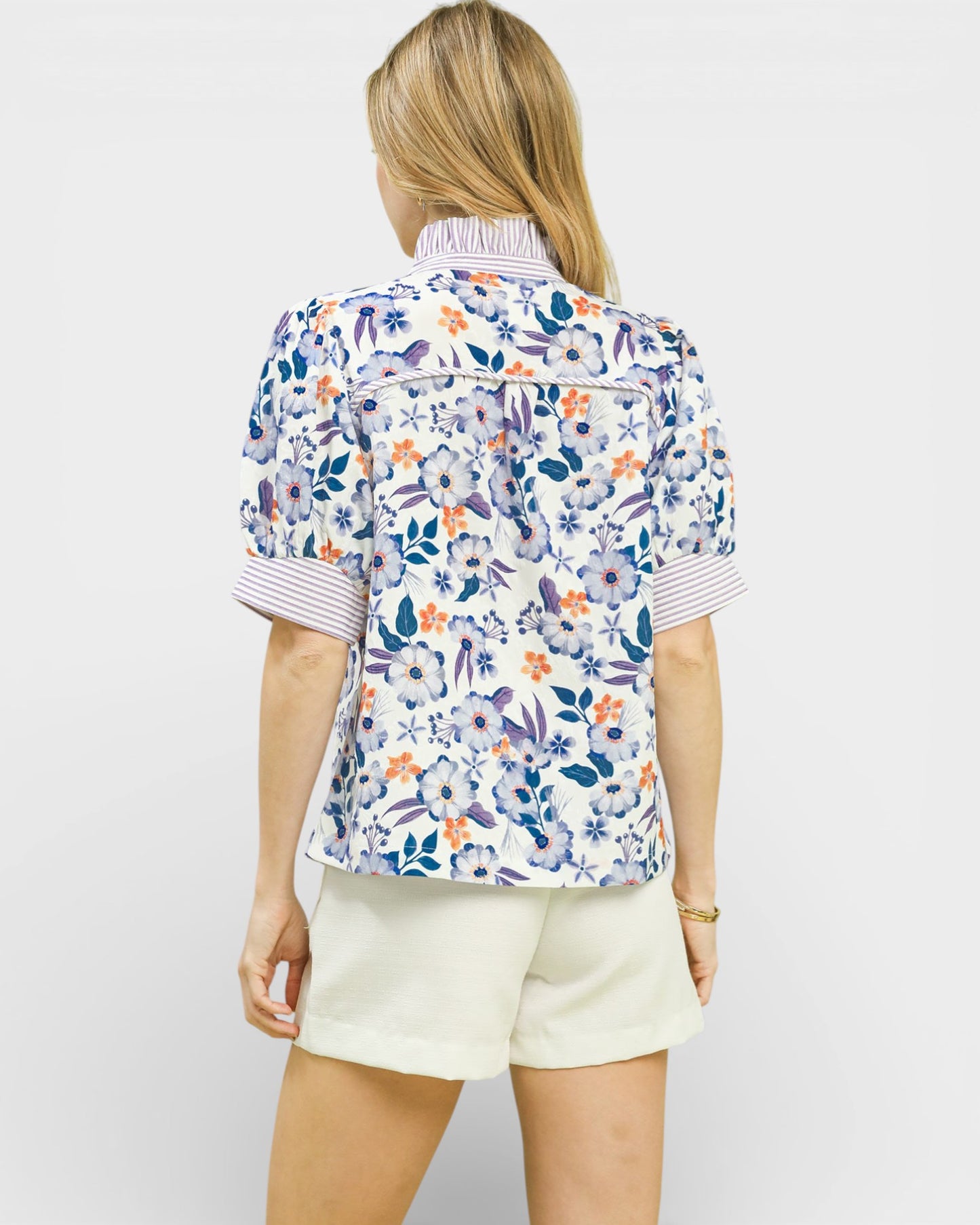 Woman wearing a floral patterned shirt and white shorts on a plain background