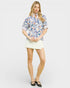 Woman wearing a floral blouse and white skirt on a plain background