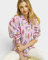 Woman wearing a pink floral blouse sitting on a white chair against a light background
