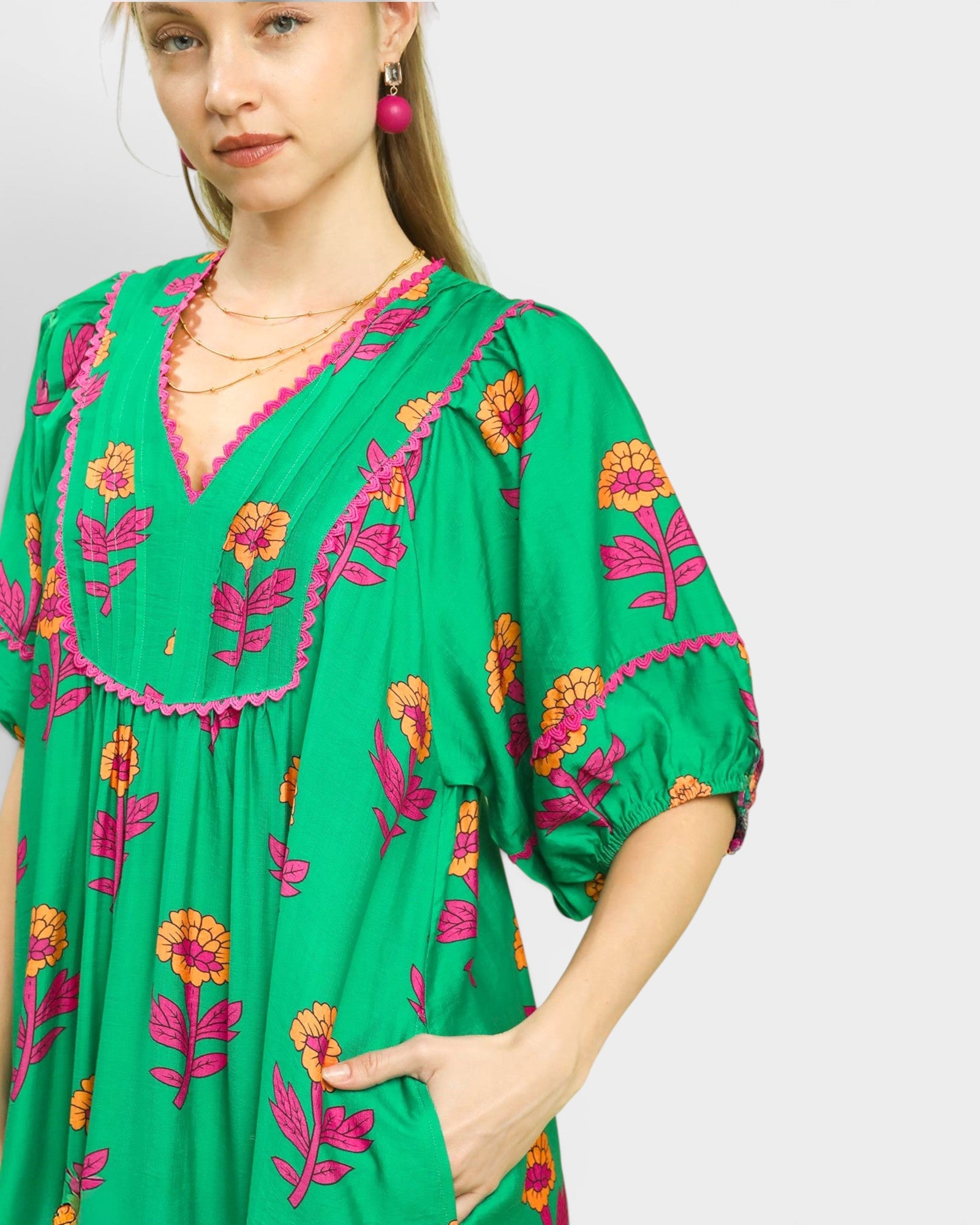 Woman wearing a green dress with floral embroidery on a plain background