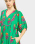 Woman wearing a green dress with floral embroidery on a plain background
