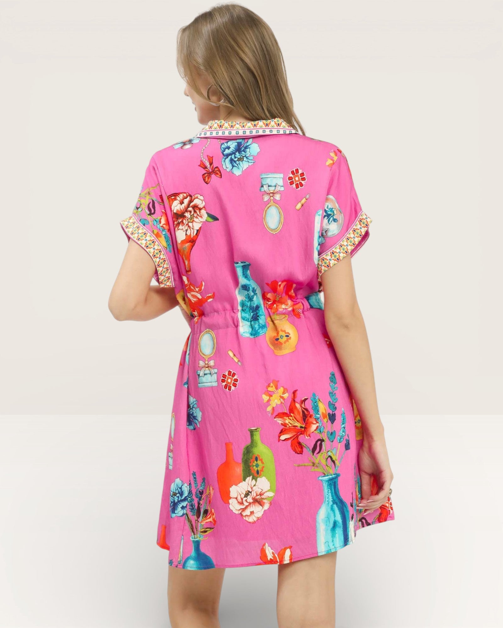 Woman wearing a pink dress with colorful floral and bottle pattern on a white background