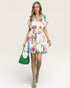 Woman wearing a colorful floral dress holding a green bag on a white background