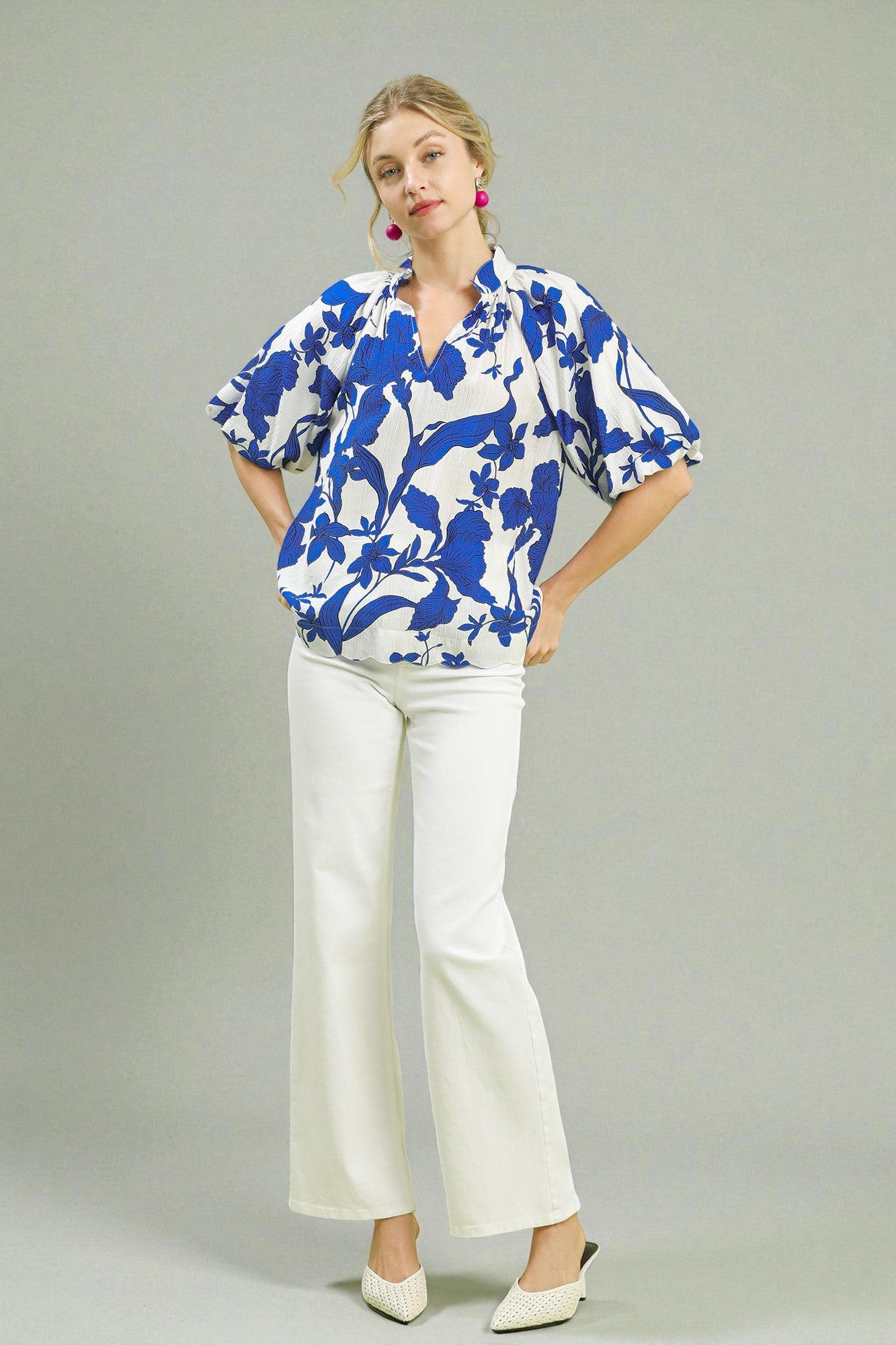 Woman wearing a blue and white floral blouse with white pants against a gray background