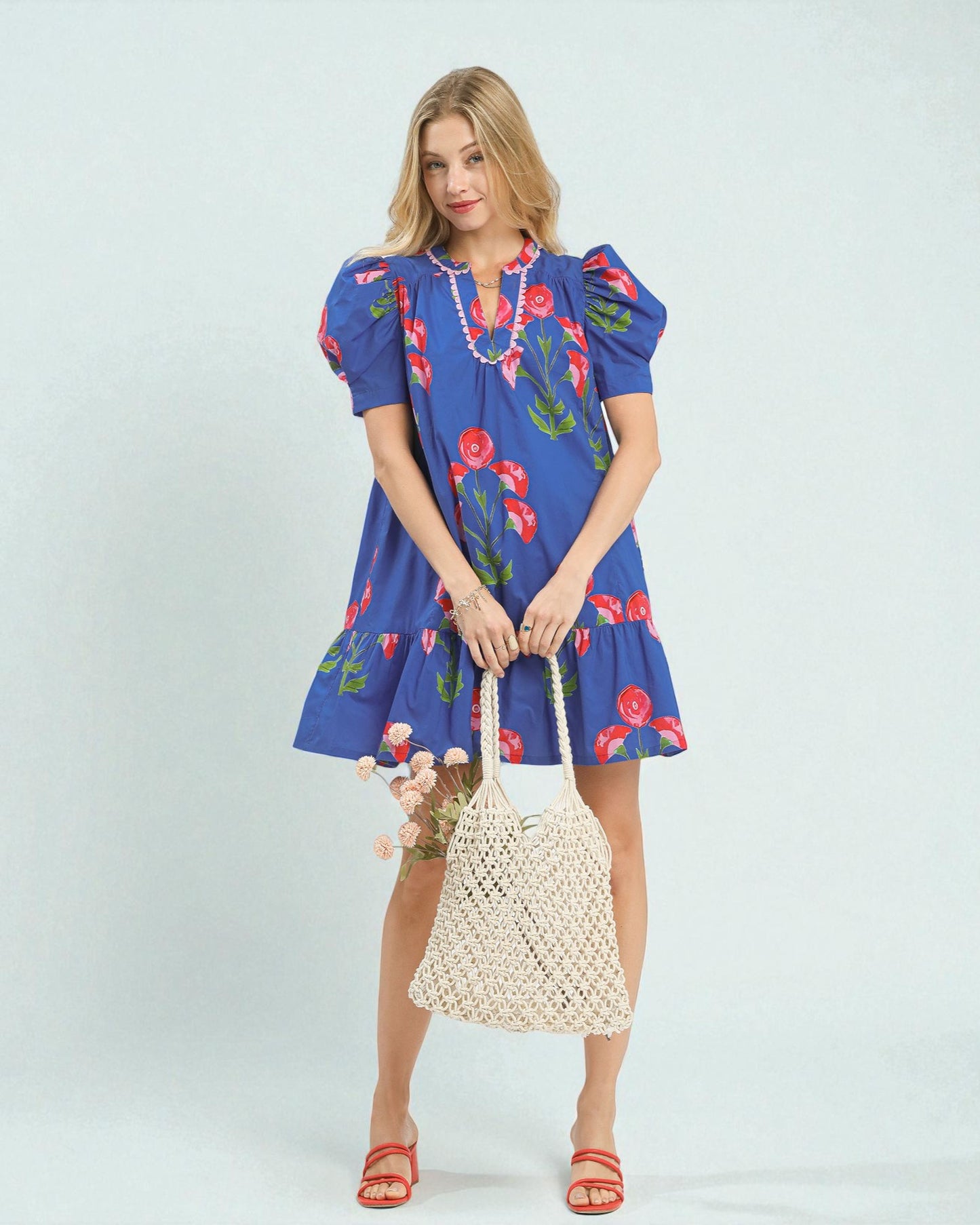 Woman wearing a blue dress with floral patterns holding a woven bag on a light blue background