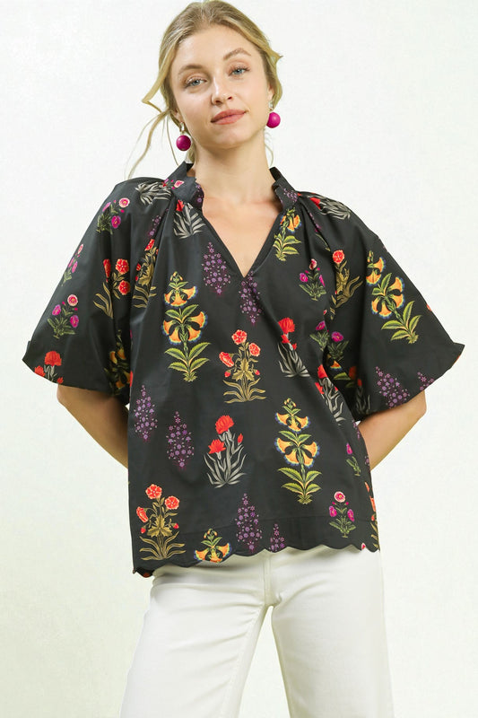 Woman wearing a black floral blouse with white pants on a plain background