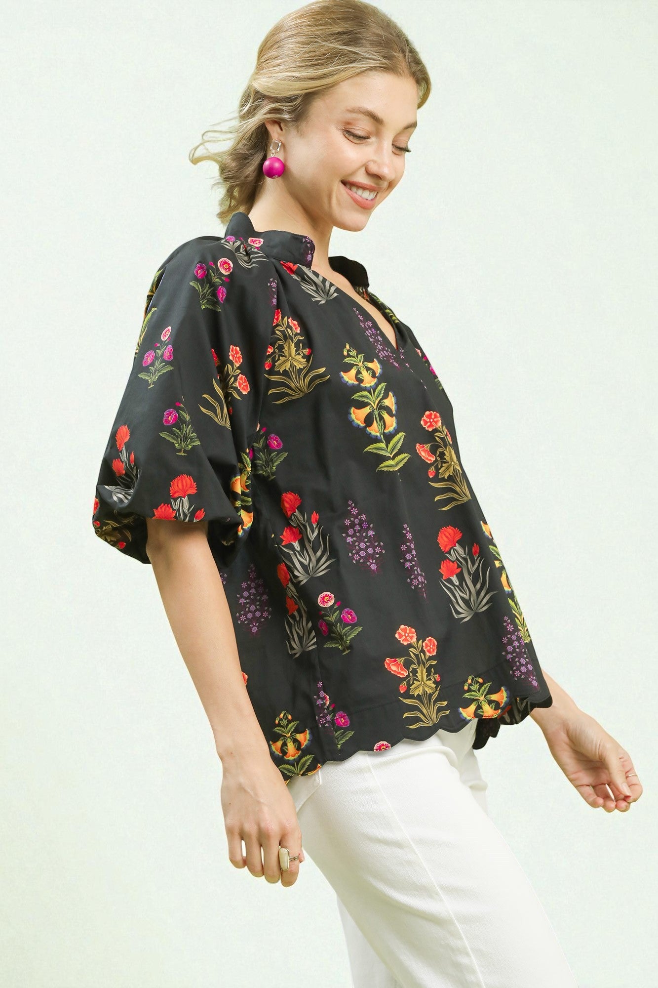 Woman wearing a black floral blouse with white pants on a light background