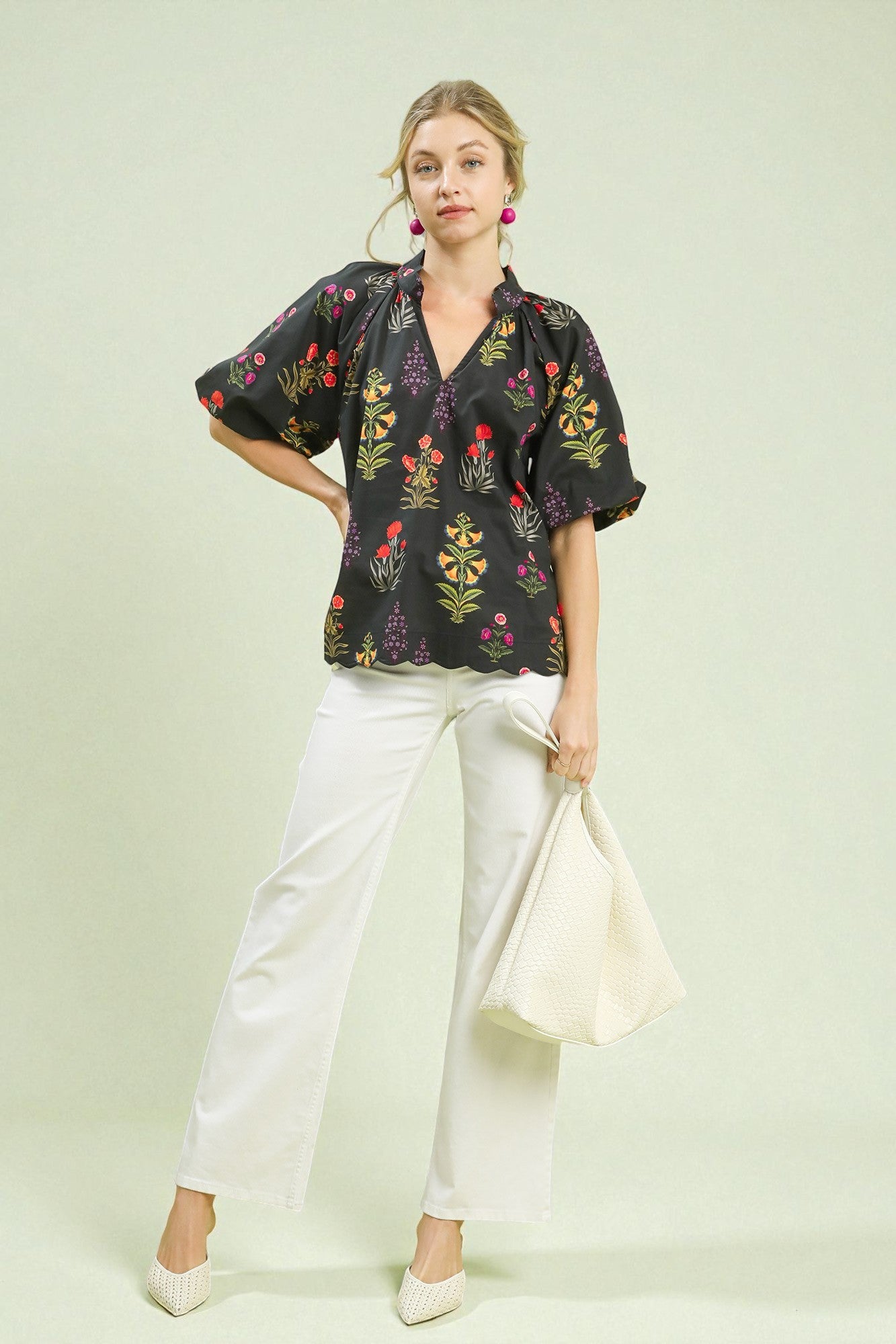 Woman wearing a black floral blouse and white pants on a light green background