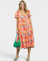 Woman wearing a colorful floral dress holding a green handbag on a white background