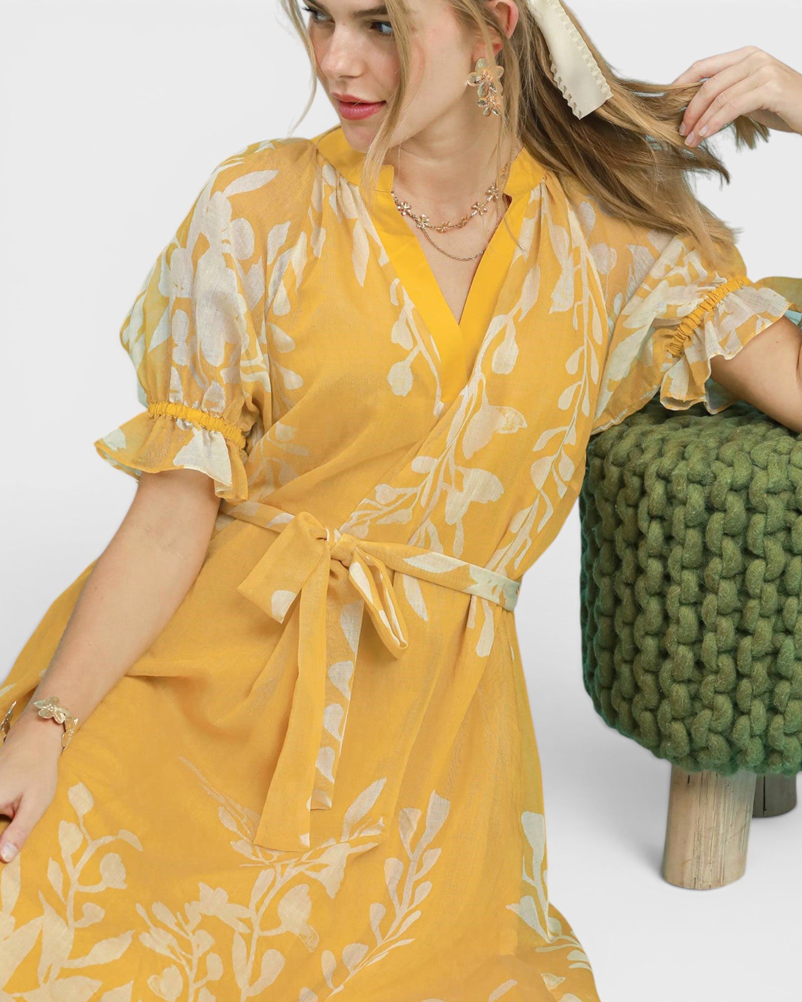 Woman wearing a yellow floral dress holding a green textured bag against a white background