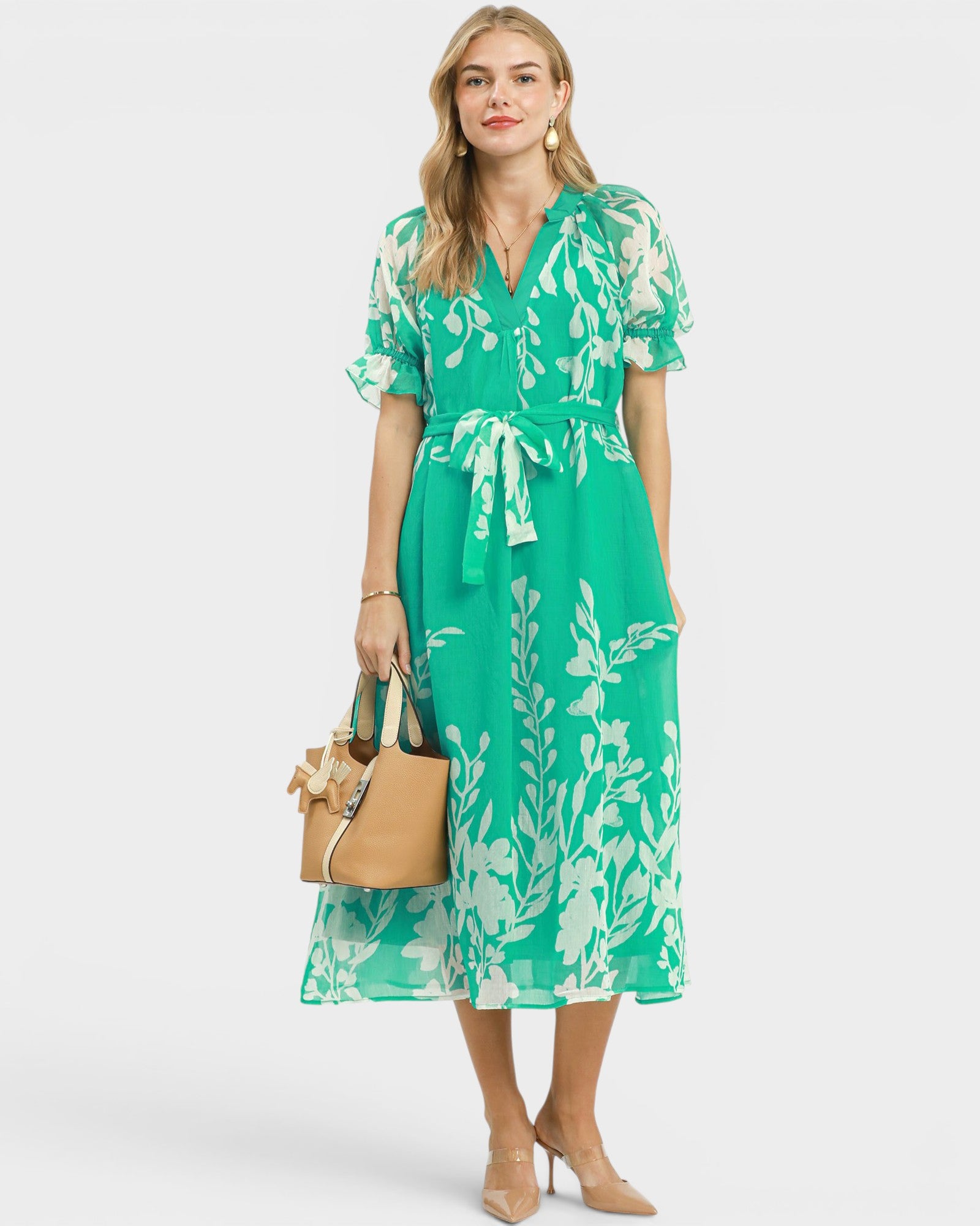 Woman wearing a green floral dress holding a beige handbag on a white background