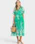 Woman wearing a green floral dress holding a beige handbag on a white background