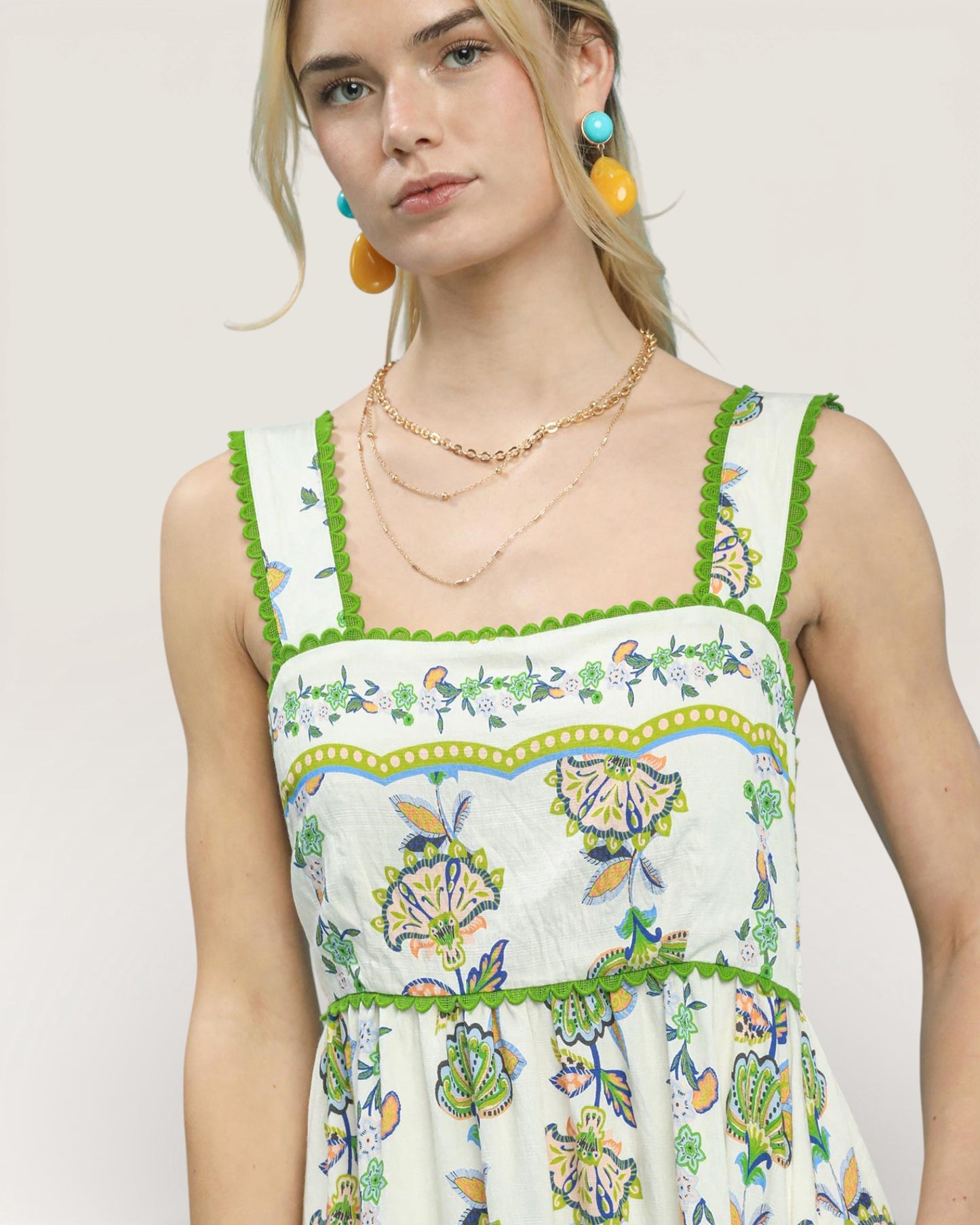 Woman wearing a floral dress with green trim on a plain background