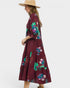 Woman wearing a burgundy dress with floral embroidery and a beige hat on a white background