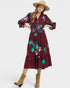 Woman wearing a burgundy dress with floral embroidery, tan hat, and boots on a white background