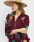 Woman wearing a burgundy dress with colorful embroidery and a beige hat on a white background