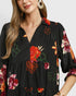 Woman wearing a black dress with colorful floral print on a plain background