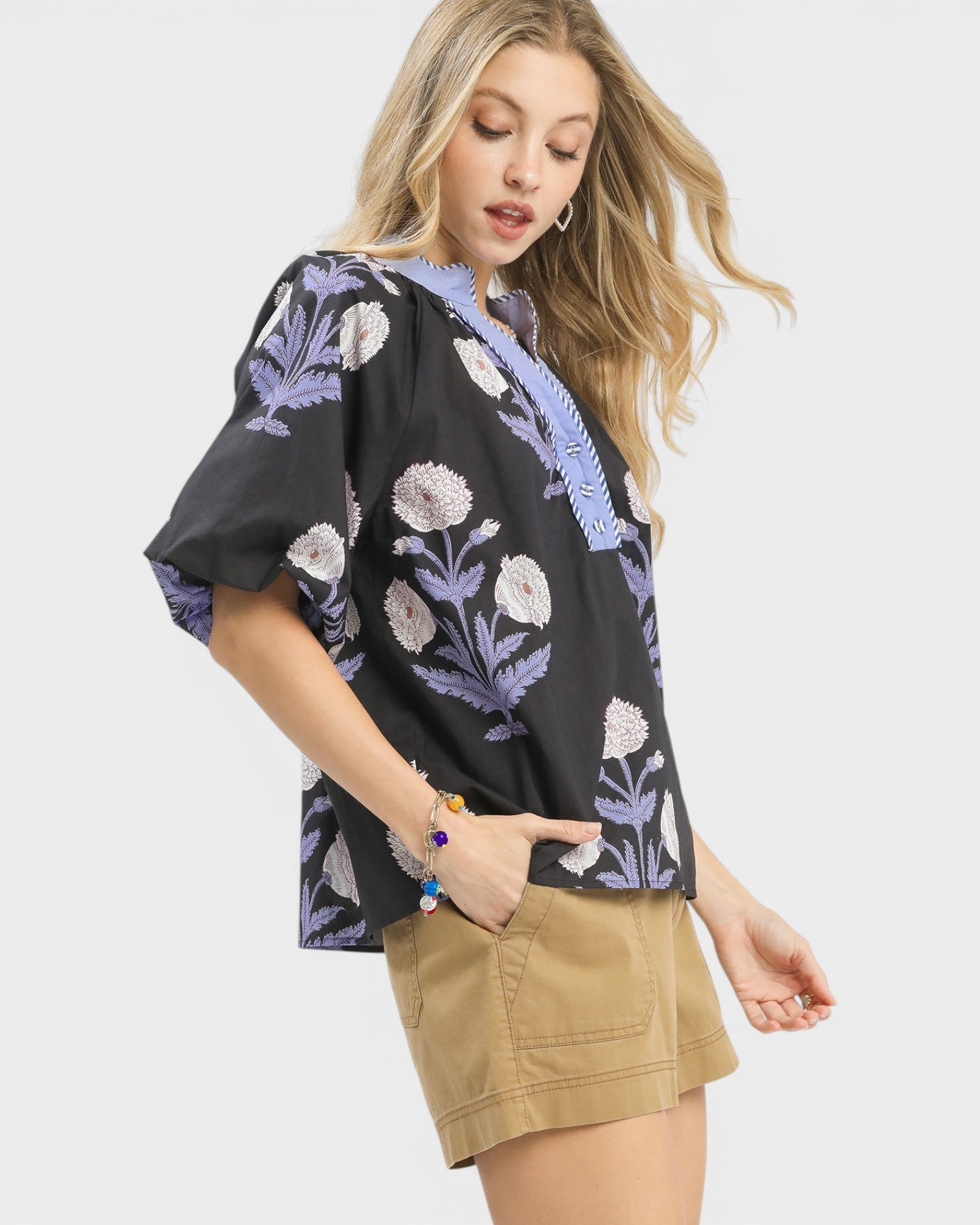 Woman wearing a black floral blouse with purple accents and beige shorts on a white background