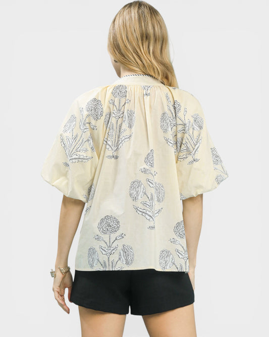 Woman wearing a light-colored blouse with floral patterns on a plain background