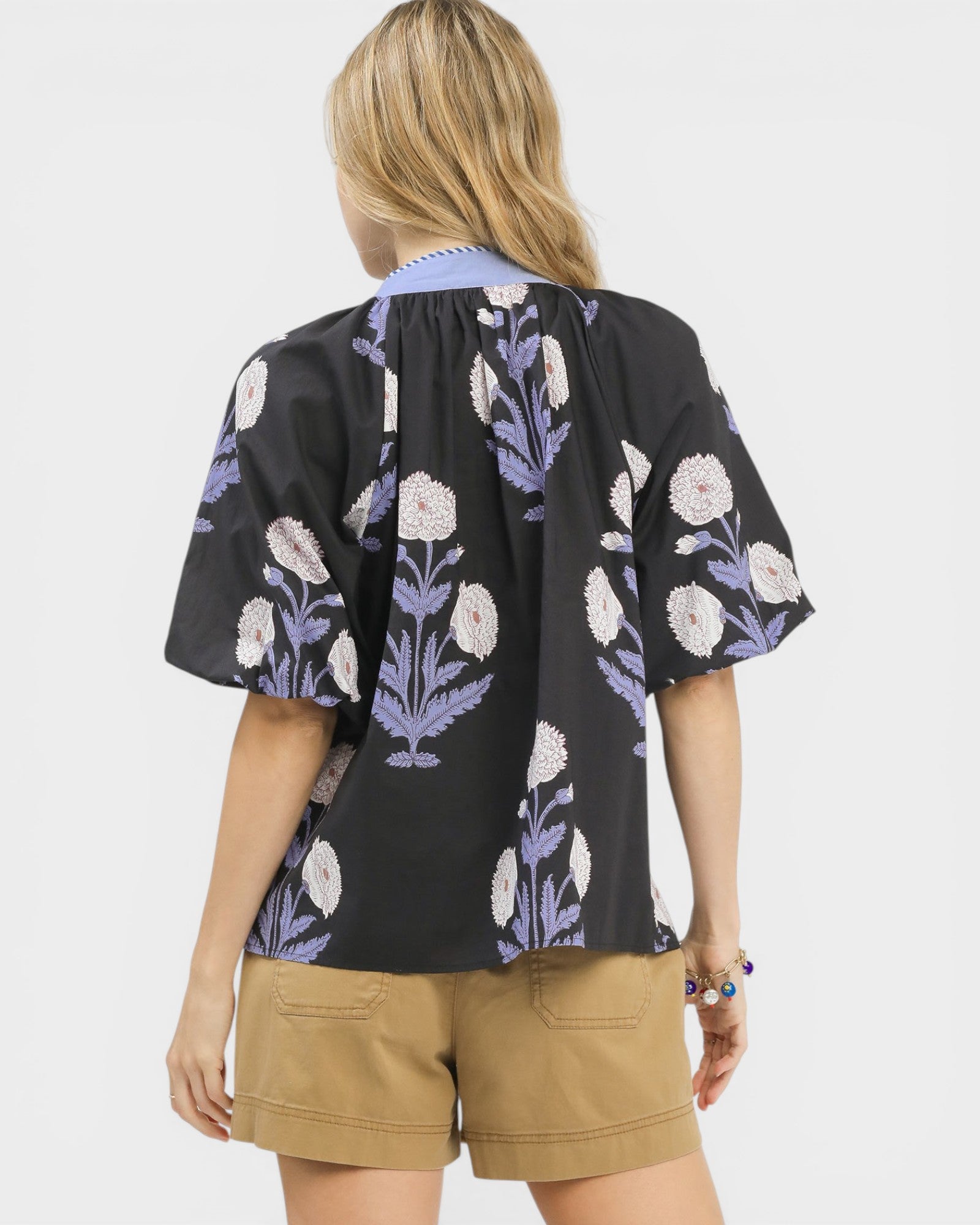 Woman wearing a black floral blouse with beige shorts on a white background