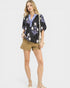 Woman wearing a black floral blouse and beige shorts on a white background
