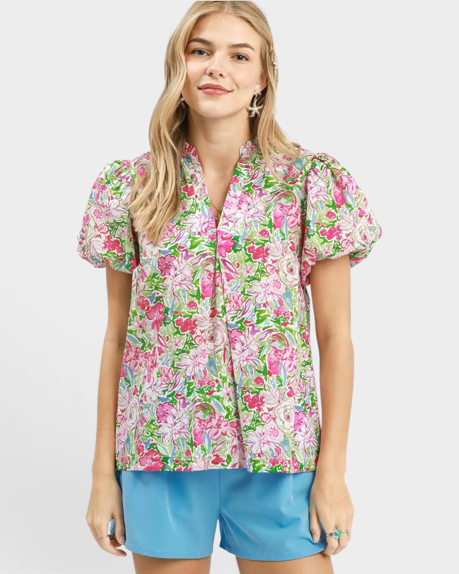 Woman wearing a colorful floral blouse and blue shorts on a white background