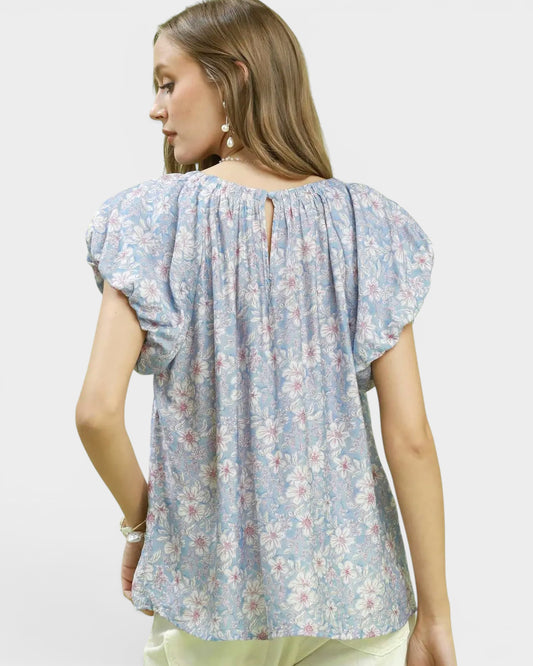 Woman wearing a light blue floral blouse with puffed sleeves on a plain background