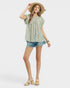 Woman wearing a green floral blouse and denim shorts on a white background