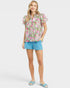 Woman wearing a floral blouse and blue shorts on a white background