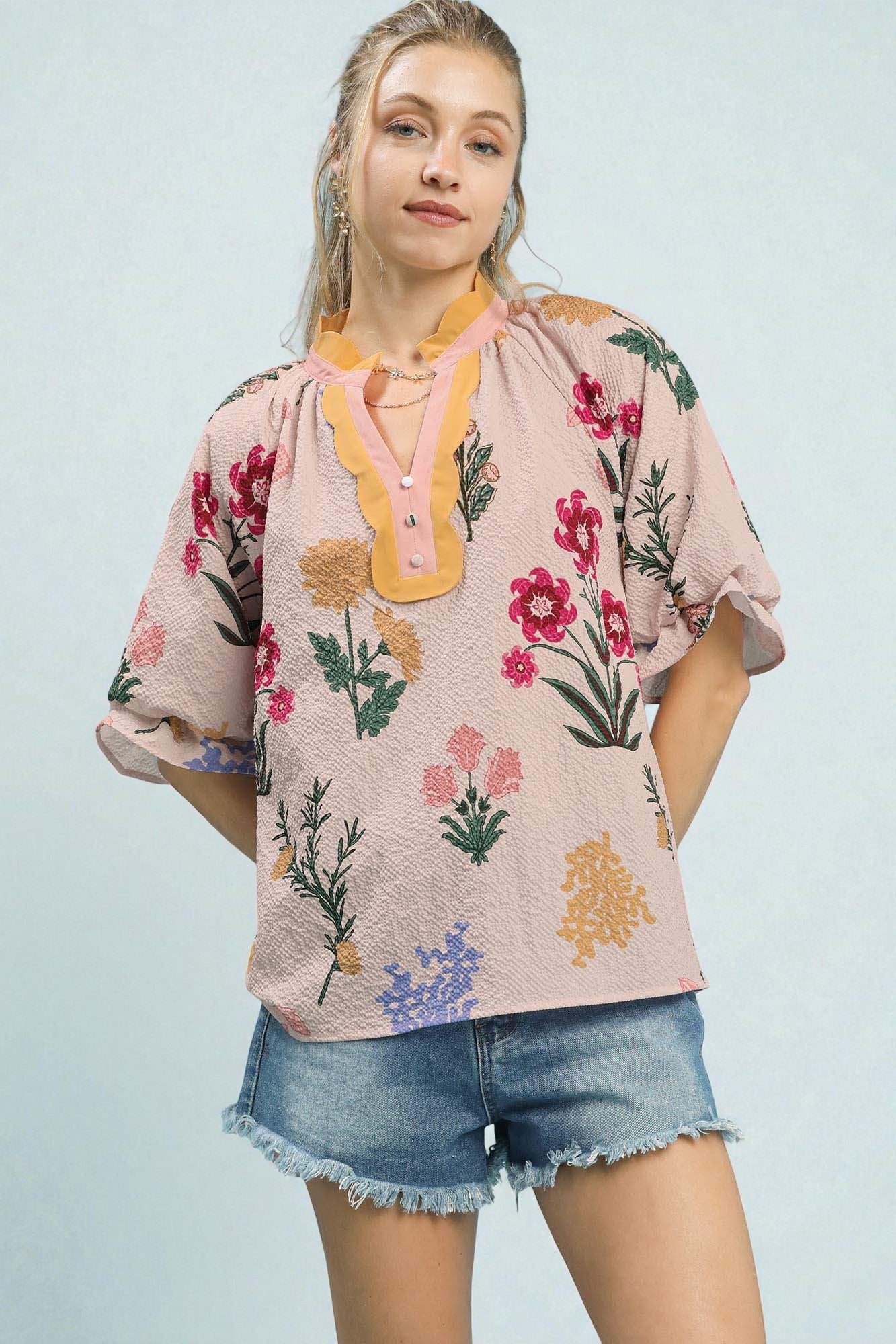 Woman wearing a floral blouse and denim shorts against a light blue background