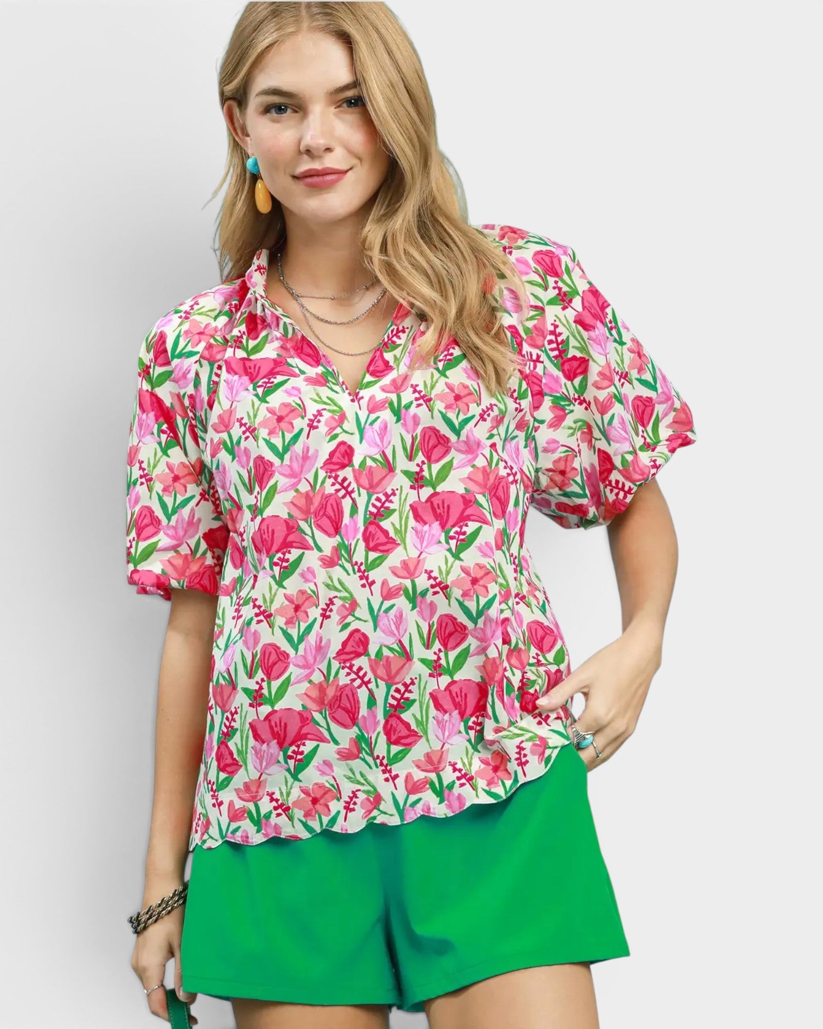 Woman wearing a floral blouse and green shorts on a plain background