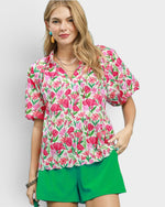 Woman wearing a floral blouse and green shorts on a plain background