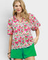 Woman wearing a floral blouse and green shorts on a plain background